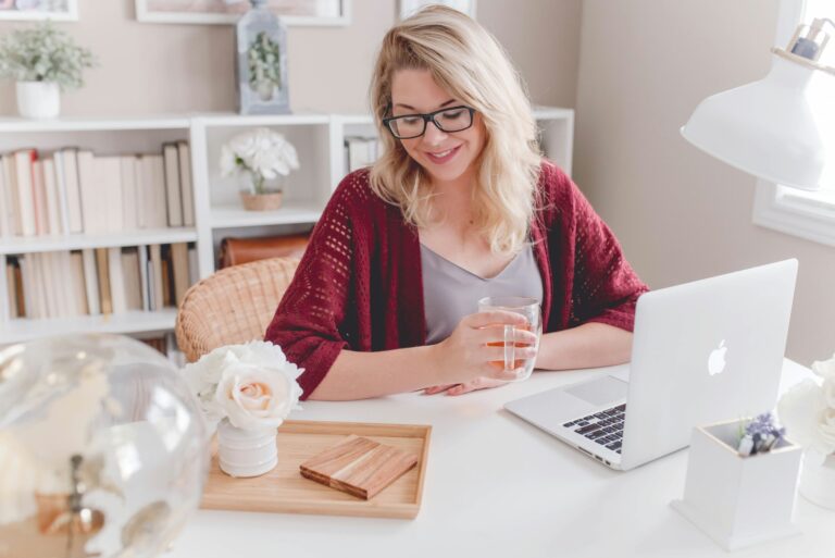 woman smiling holding glass mug sitting beside table with macbook